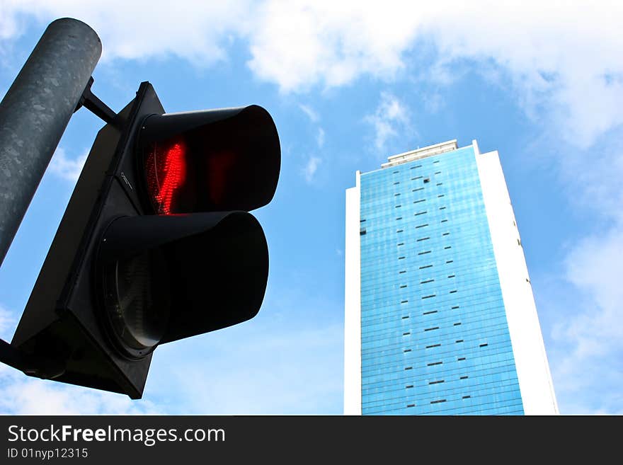 A traffic light with a stop sign before a tall sky scraper