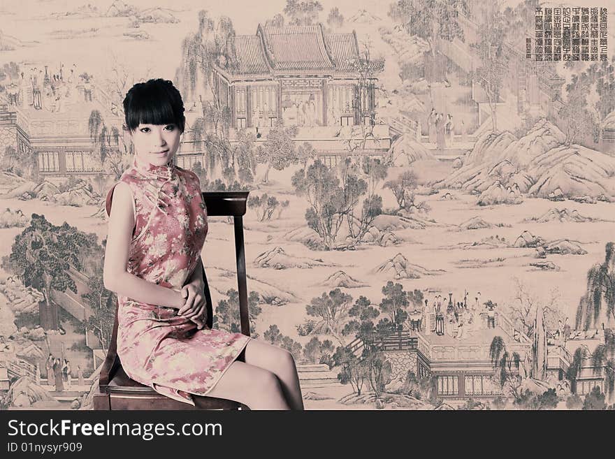 A Chinese girl in traditional dress sits in front of a Chinese old painting. Chinese characters on the picture are China's ancient poesy. Usually there is a piece of poesy in the old painting above of China. Adjust the tone on later stage in picture.