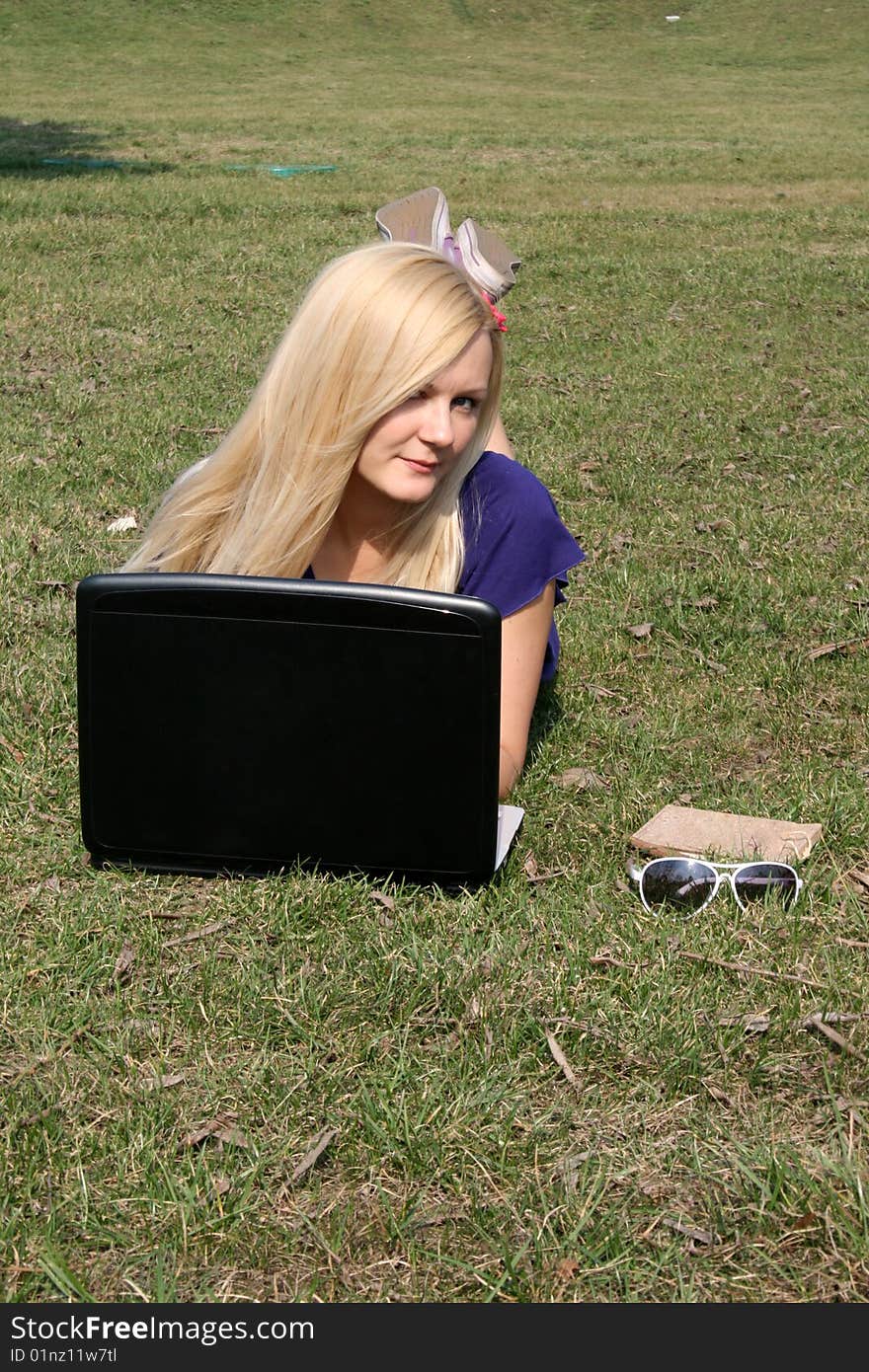 Smiling girl with a laptop lying on grass