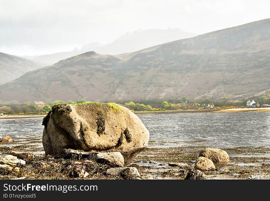 Rock on Lochranza with mountains in the haze. Rock on Lochranza with mountains in the haze