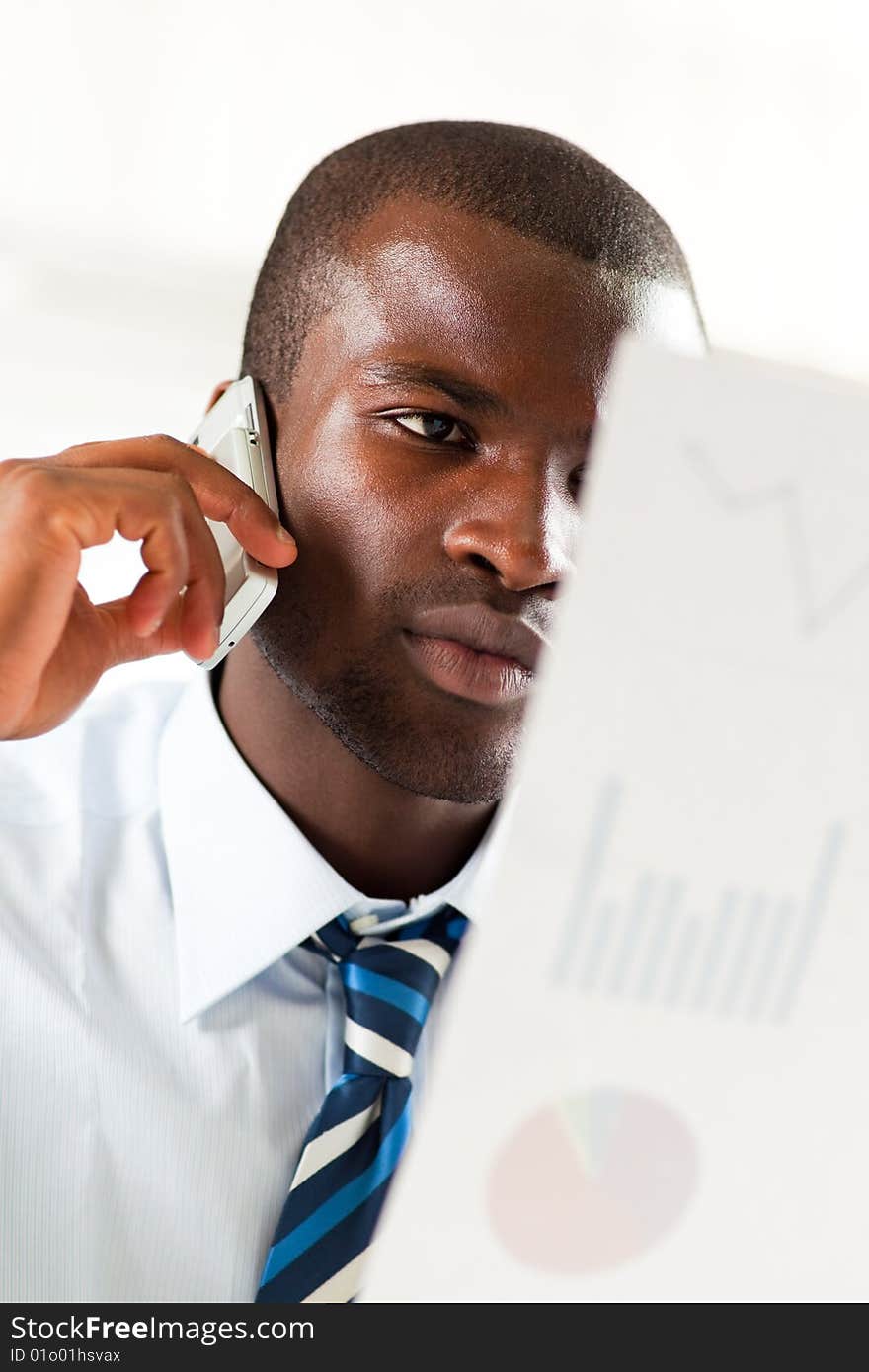 Young adult afro-american businessman examining charts and talking on the phone. Young adult afro-american businessman examining charts and talking on the phone