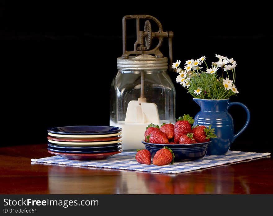 Fresh strawberries in cobalt blue bowl, colorful plates stacked to the side and antique butter churn filled with cream in background. Fresh strawberries in cobalt blue bowl, colorful plates stacked to the side and antique butter churn filled with cream in background