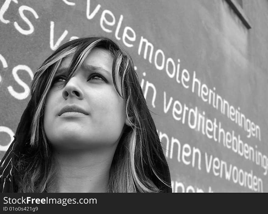 Girl standing in front of a wall with writings on it.
The words on the background means in Dutch: many beautiful memories, to have sorrow, find words.