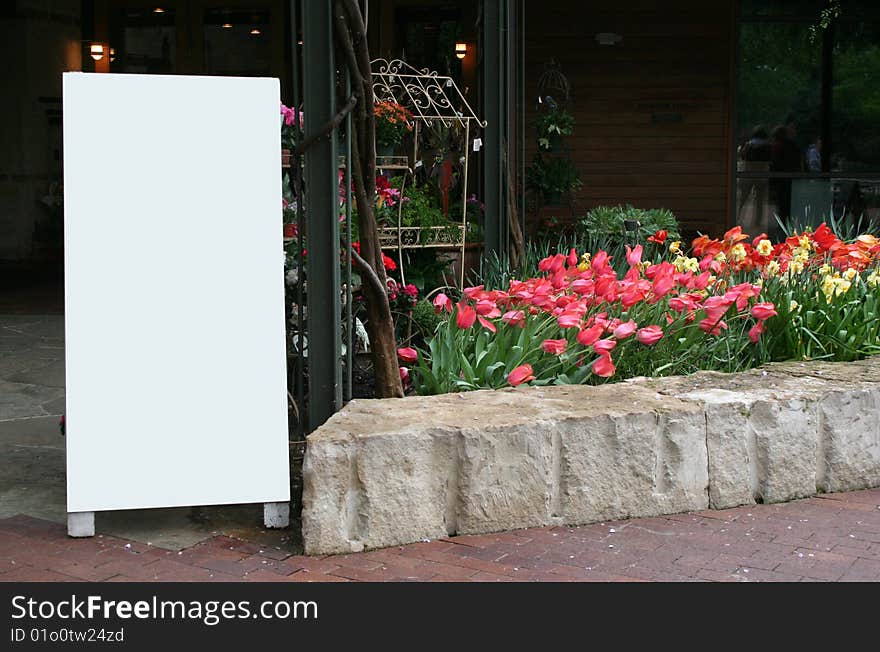 A blank sign stands next to a flower bed full of tulips. A blank sign stands next to a flower bed full of tulips.