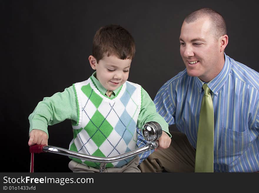 Proud father looking at young toddler son on a tricycle. Proud father looking at young toddler son on a tricycle