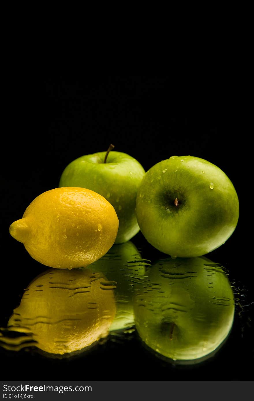 Apple and lemon on mirror over black