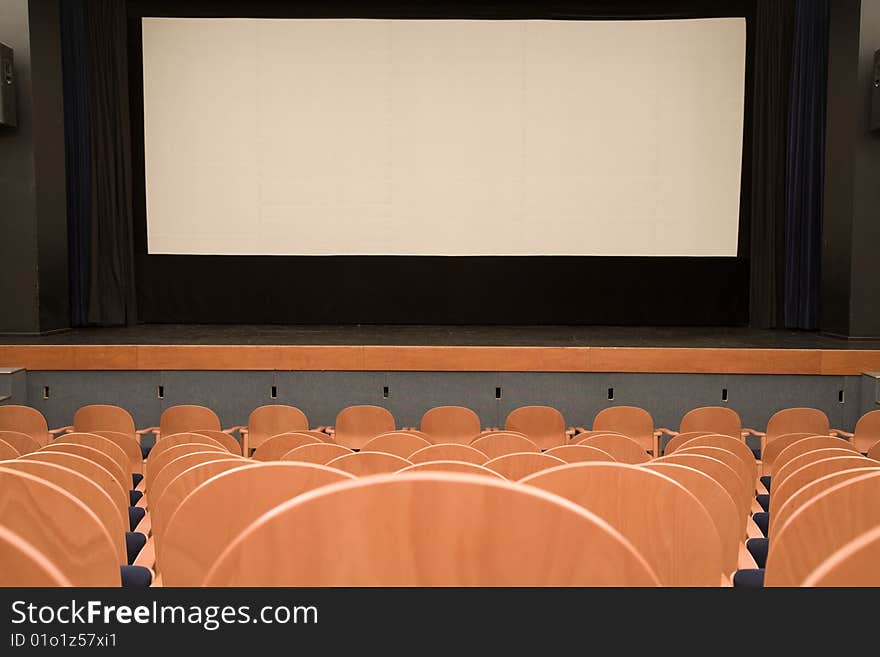 Empty cinema auditorium with line of wooden chairs and projection screen. Ready for adding your own picture.
