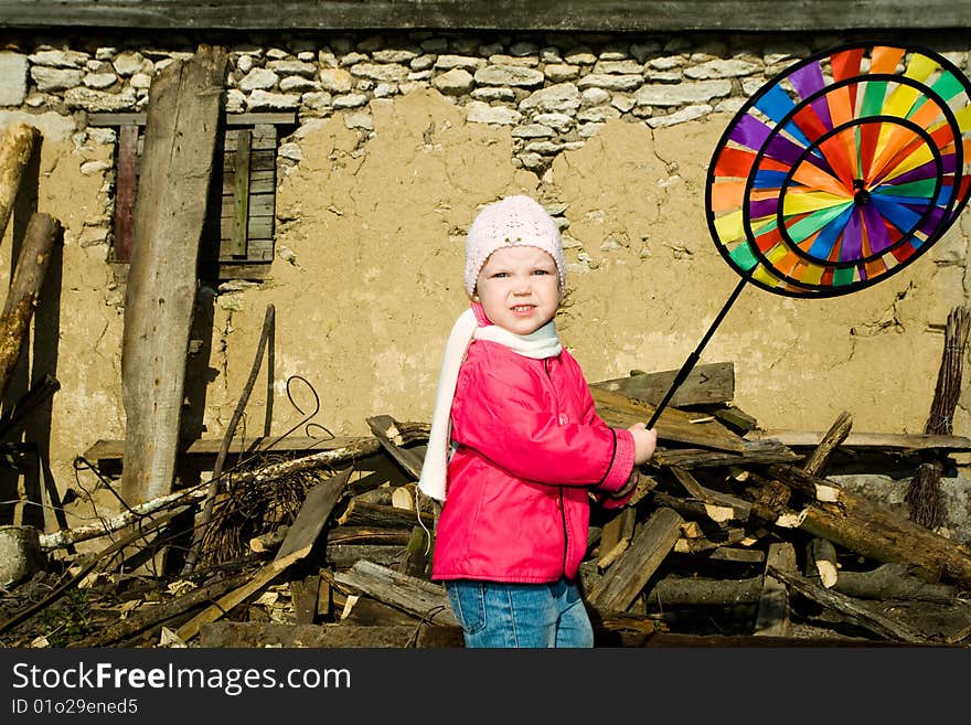 A pretty  little  girl playing  with  her plaything on a background of an old  barn in the countryside. A pretty  little  girl playing  with  her plaything on a background of an old  barn in the countryside