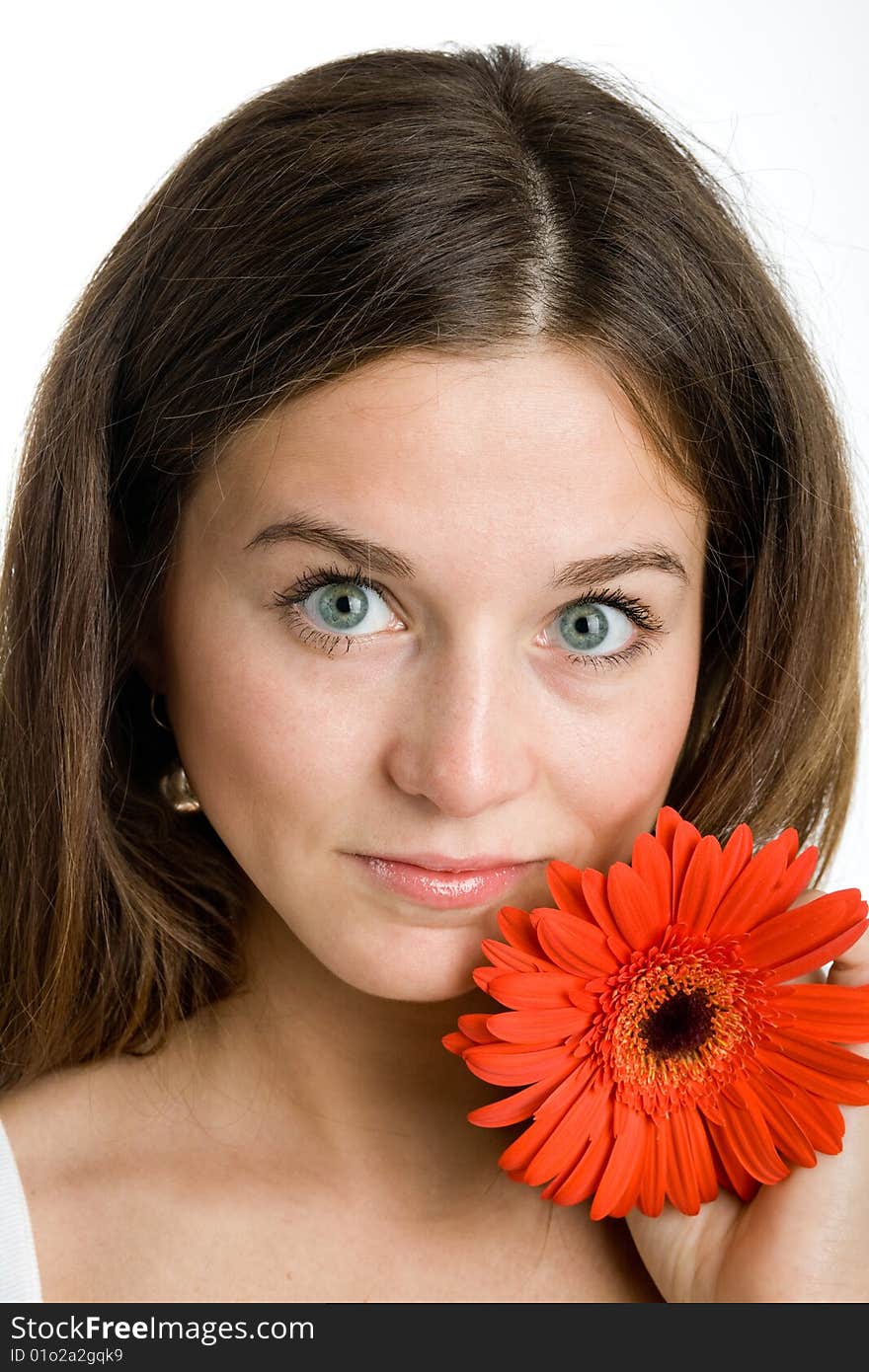 A smiling beautiful young woman in a white dress with a bright red flower near her face. A smiling beautiful young woman in a white dress with a bright red flower near her face