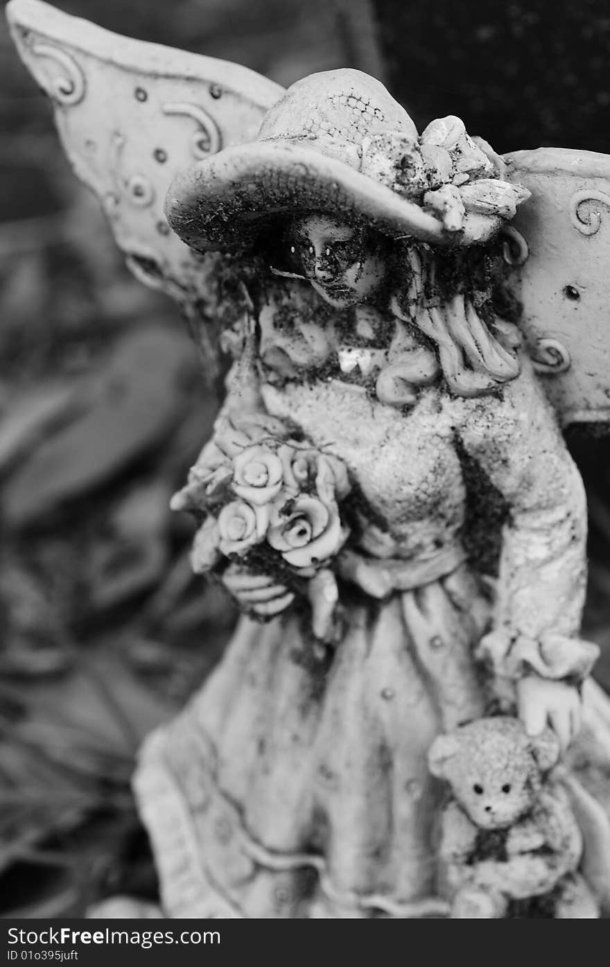 Creepy black and white statue of a young angel holding flowers and a teddy bear. Creepy black and white statue of a young angel holding flowers and a teddy bear