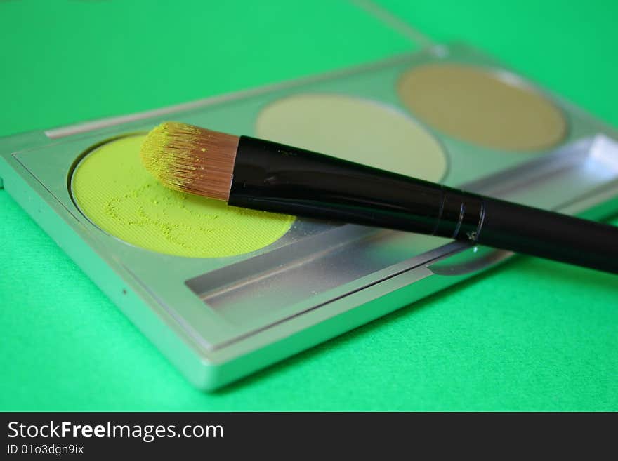 A set of three different green eyeshadow with brush and green background. A set of three different green eyeshadow with brush and green background