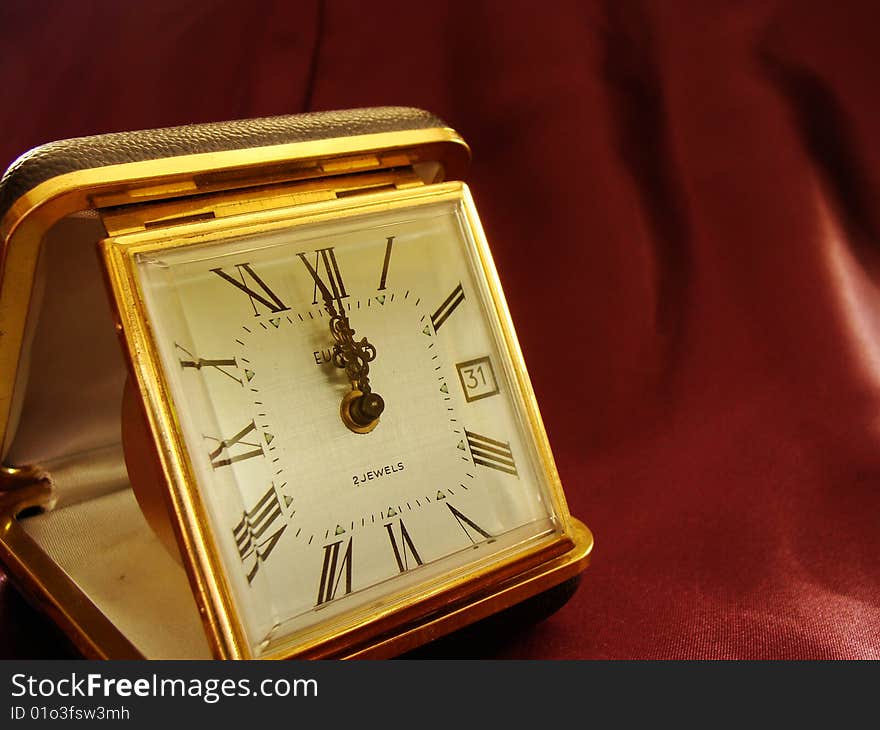 Concept of time measuring, golden clock on dark red fabric background