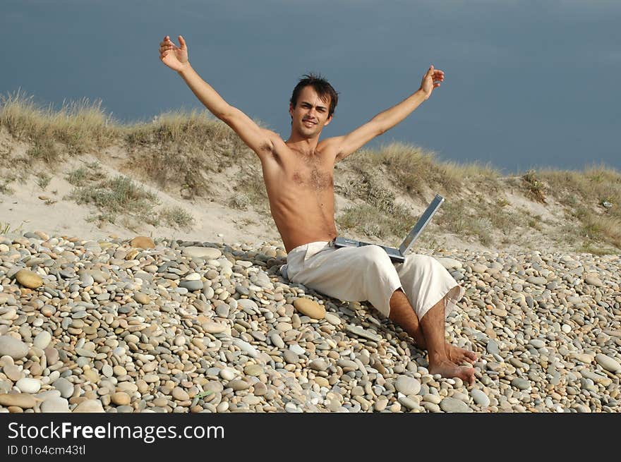 Handsome young with computer on the beach without a t-shirt. Handsome young with computer on the beach without a t-shirt