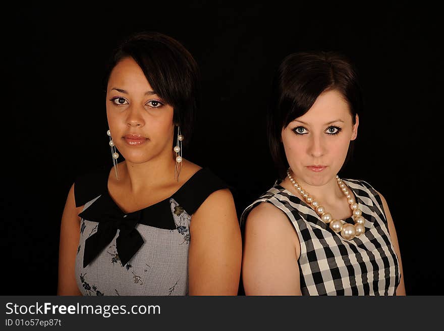 A portrait of two beautiful woman in dresses, on black studio background. A portrait of two beautiful woman in dresses, on black studio background.