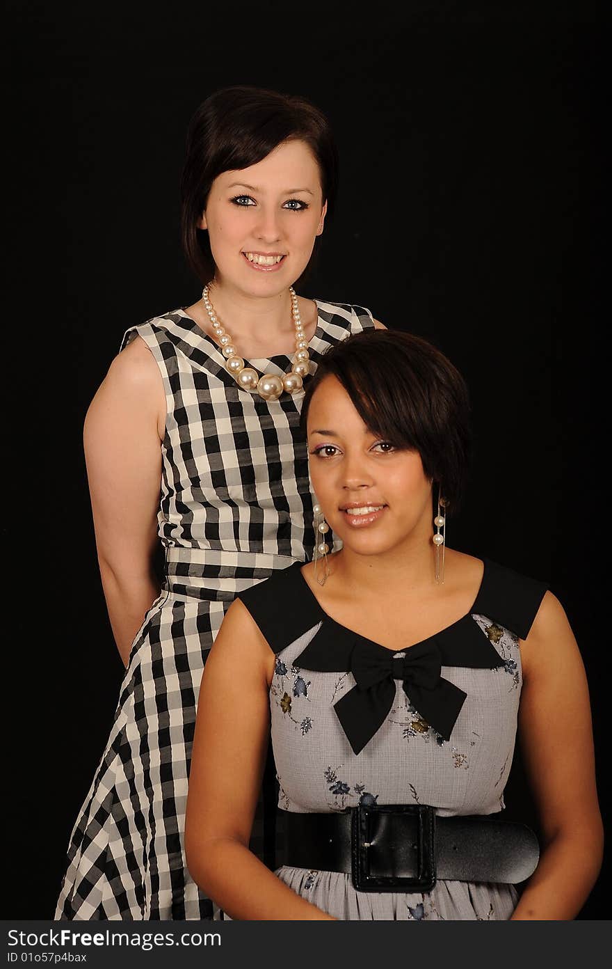 A portrait of two beautiful woman in dresses, on black studio background. A portrait of two beautiful woman in dresses, on black studio background.