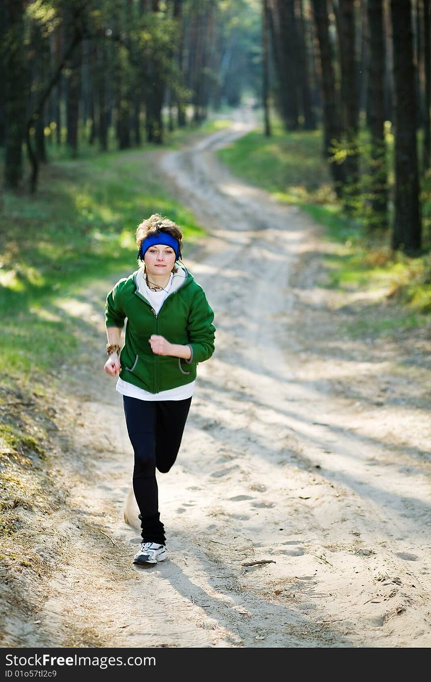 Pretty young girl runner in the forest while listening to music.