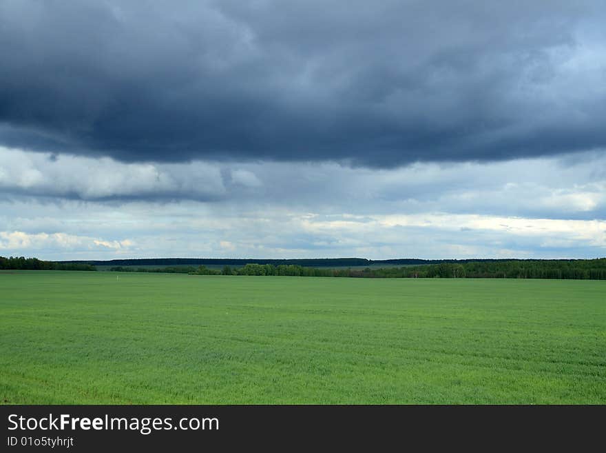 Panoramic landscape with green field under storm clouds