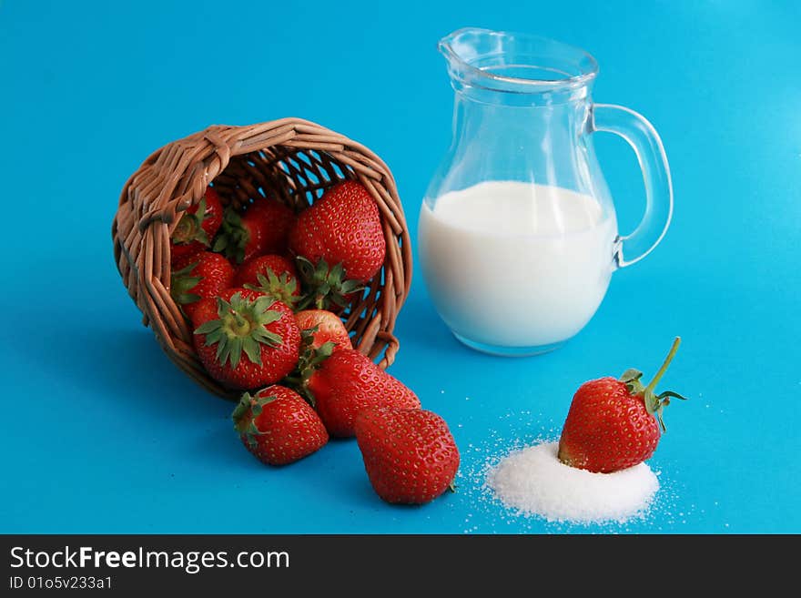 Strawberries in a wicker basket, jug of milk or yoghurt and sugar on blue background. Strawberries in a wicker basket, jug of milk or yoghurt and sugar on blue background.