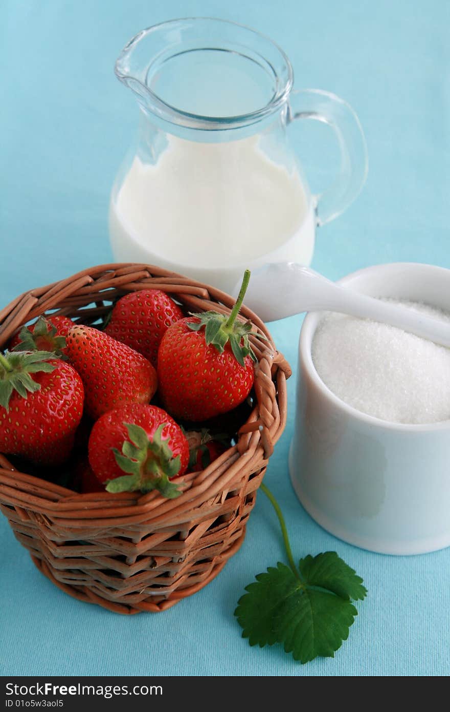 Strawberries in a wicker basket, jug of milk or yoghurt and sugar on blue background. Strawberries in a wicker basket, jug of milk or yoghurt and sugar on blue background.