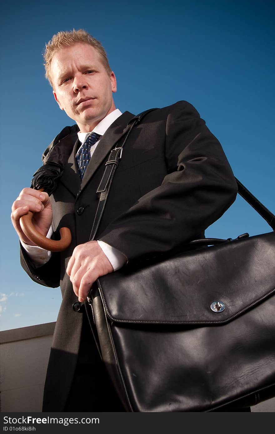 A businessman holding a briefcase and umbrella outside. A businessman holding a briefcase and umbrella outside