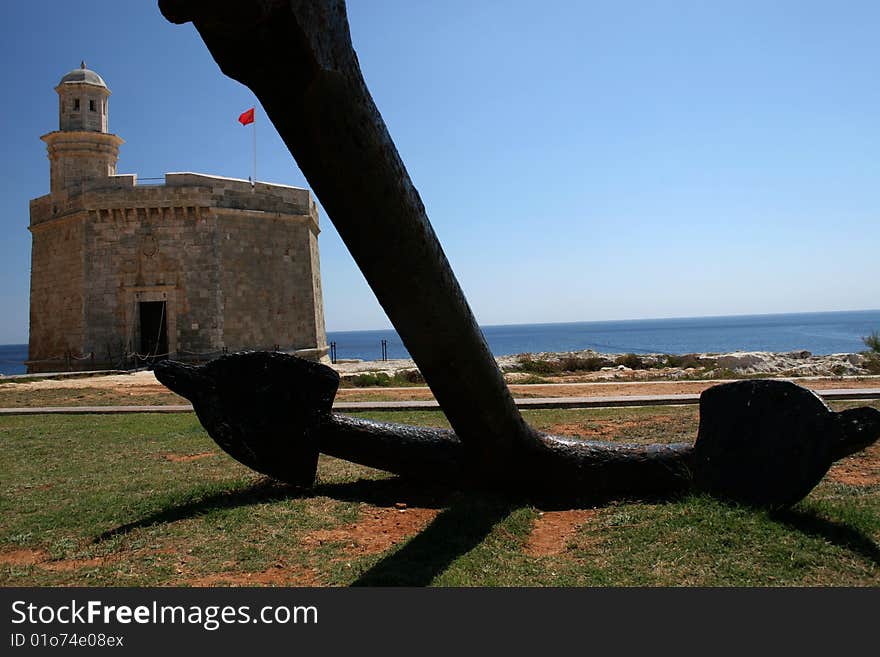 Anchor with a fortress in a background on a coast. Anchor with a fortress in a background on a coast