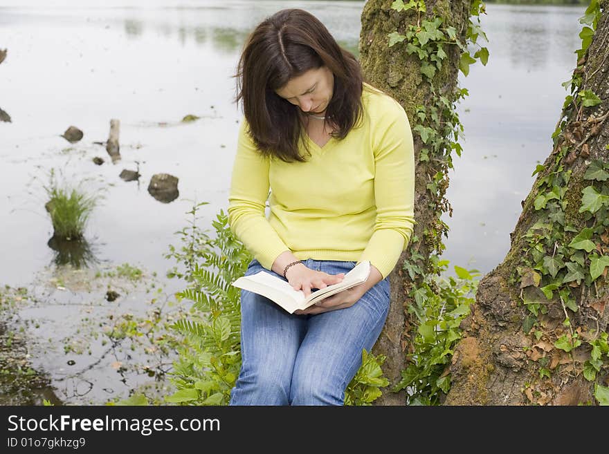 A young woman reading a book sited on a park