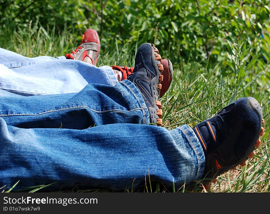 Two people wearing jeans and running shoes laying in the green grass. Two people wearing jeans and running shoes laying in the green grass