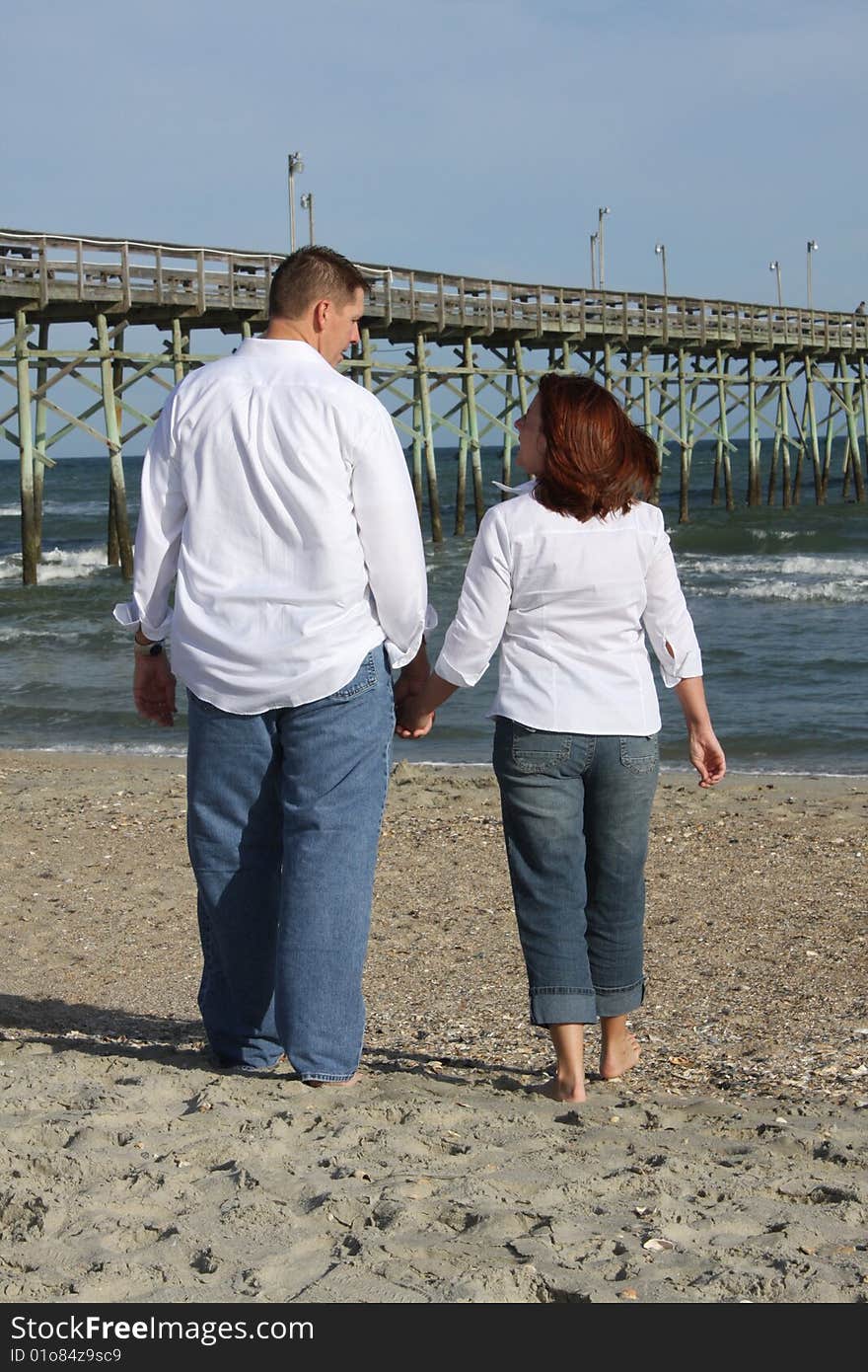 A young couple walking on the beach barefoot sharing a moment. A young couple walking on the beach barefoot sharing a moment