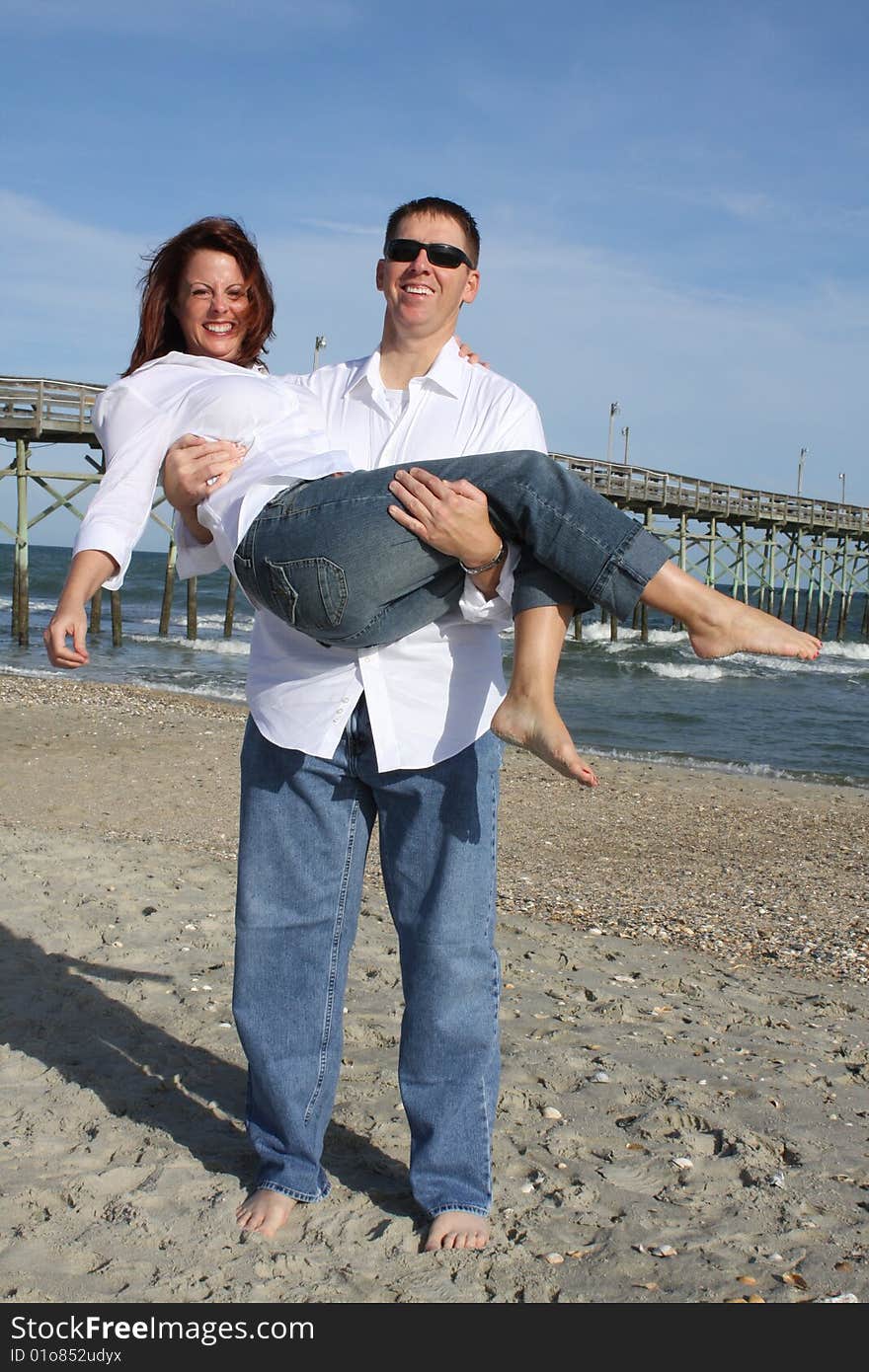 A young couple enjoying time together at the beach. The man is holding the woman in his arms. A young couple enjoying time together at the beach. The man is holding the woman in his arms.