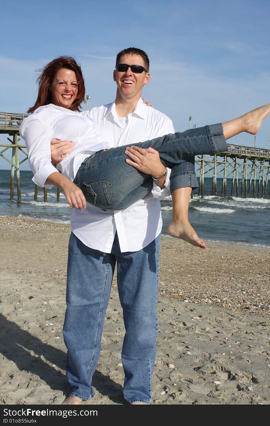 A young couple enjoying time together at the beach.  The man is holding the woman in his arms. A young couple enjoying time together at the beach.  The man is holding the woman in his arms.