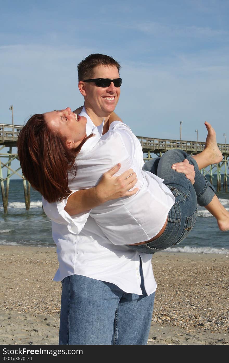 A young couple enjoying time together at the beach.  The man is holding the woman in his arms and they are both laughing. A young couple enjoying time together at the beach.  The man is holding the woman in his arms and they are both laughing.