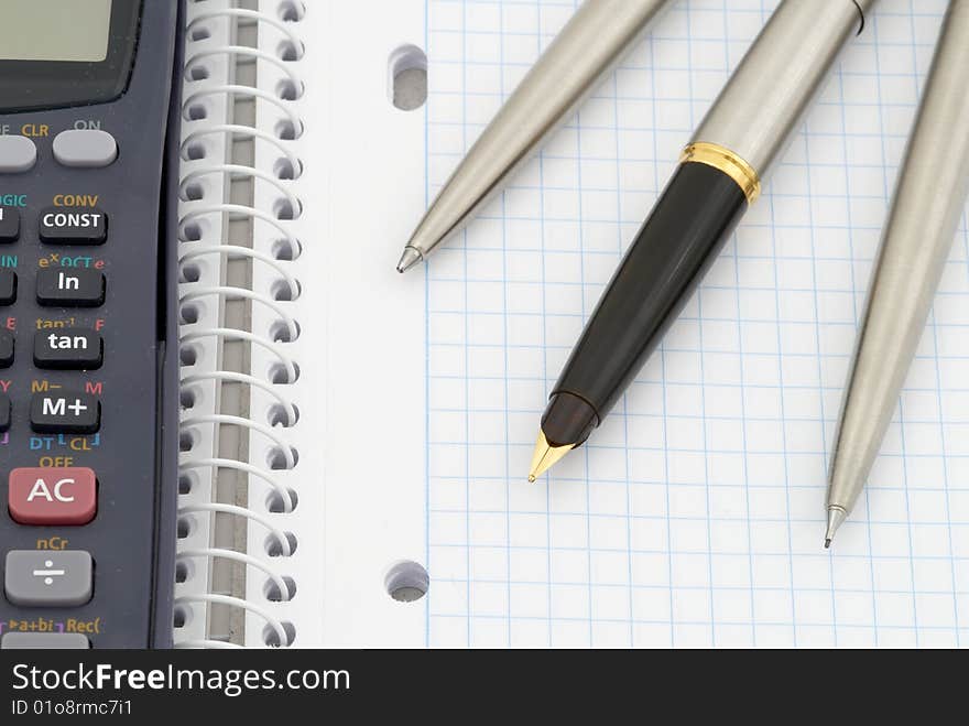 Spiral notebook with blue grid. Calculator, pen, pencil and fountain pen. Selective focus