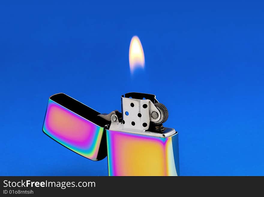 Golden metal cigarette lighter with flame on blue background. Selective focus. Golden metal cigarette lighter with flame on blue background. Selective focus