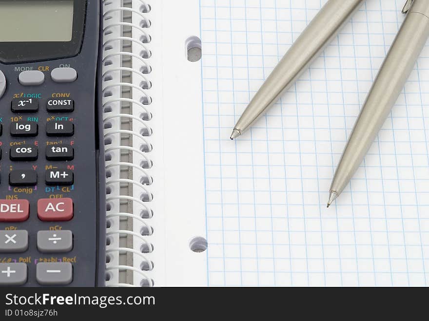 Spiral notebook with blue grid. Calculator, pen and  pencil. Selective focus