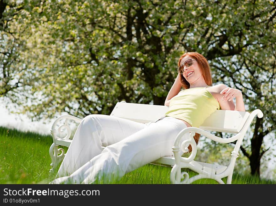 Red hair woman relaxing on white bench in summer meadow; shallow DOF. Red hair woman relaxing on white bench in summer meadow; shallow DOF