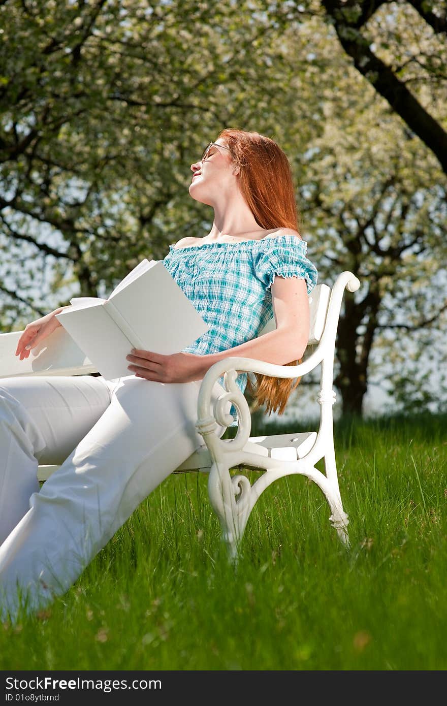 Red hair woman relaxing on white bench in summer meadow; shallow DOF. Red hair woman relaxing on white bench in summer meadow; shallow DOF