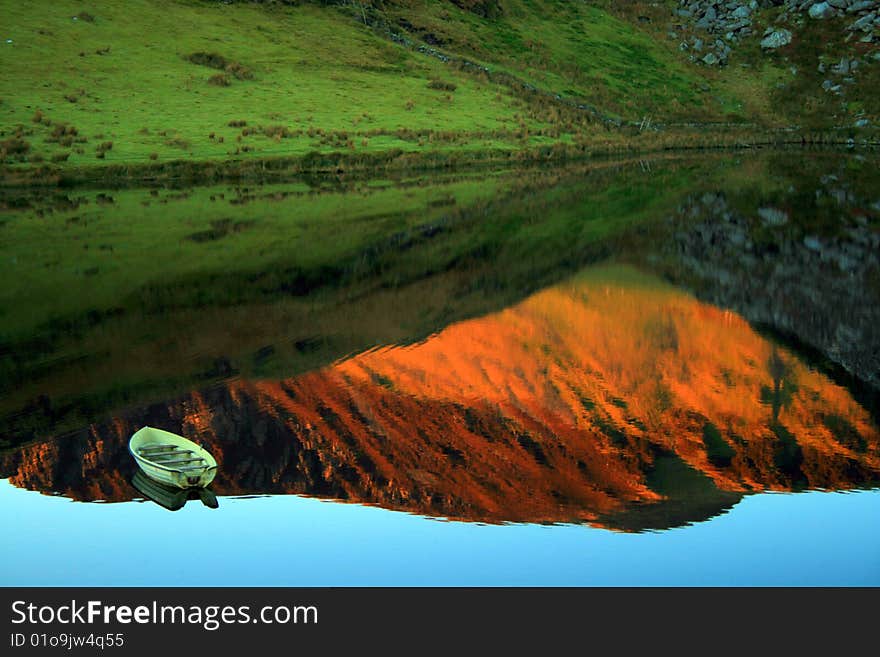 A lonely fishingboat on LLyn y Dywarchen lake in Snowdonia. The mountains are reflected in the lake at sunset. A lonely fishingboat on LLyn y Dywarchen lake in Snowdonia. The mountains are reflected in the lake at sunset.