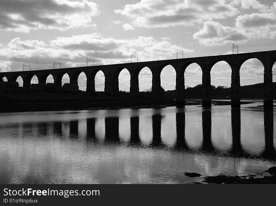 Wide black and white shot of the Royal Border Railway Bridge at Berwick Upon Tweed, taken as a silhoutte against a semi cloudy sky with the bridge reflecting in the water. Wide black and white shot of the Royal Border Railway Bridge at Berwick Upon Tweed, taken as a silhoutte against a semi cloudy sky with the bridge reflecting in the water.