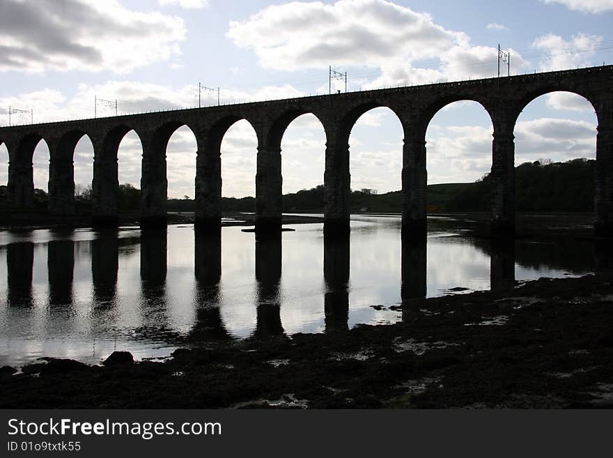 A silhouette of the Royal Broder Railway Bridge at Berwick Upon Tweed in Britain, shot against a cloudy blue sky and the piers reflecting in the water. A silhouette of the Royal Broder Railway Bridge at Berwick Upon Tweed in Britain, shot against a cloudy blue sky and the piers reflecting in the water.