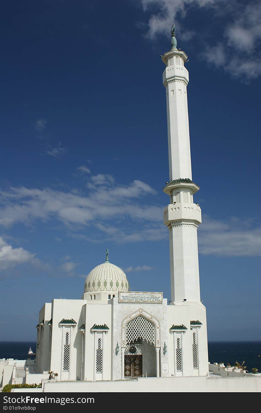 White marble mosque on the coast of Gibraltar, under a blue sky with the sea in the background.