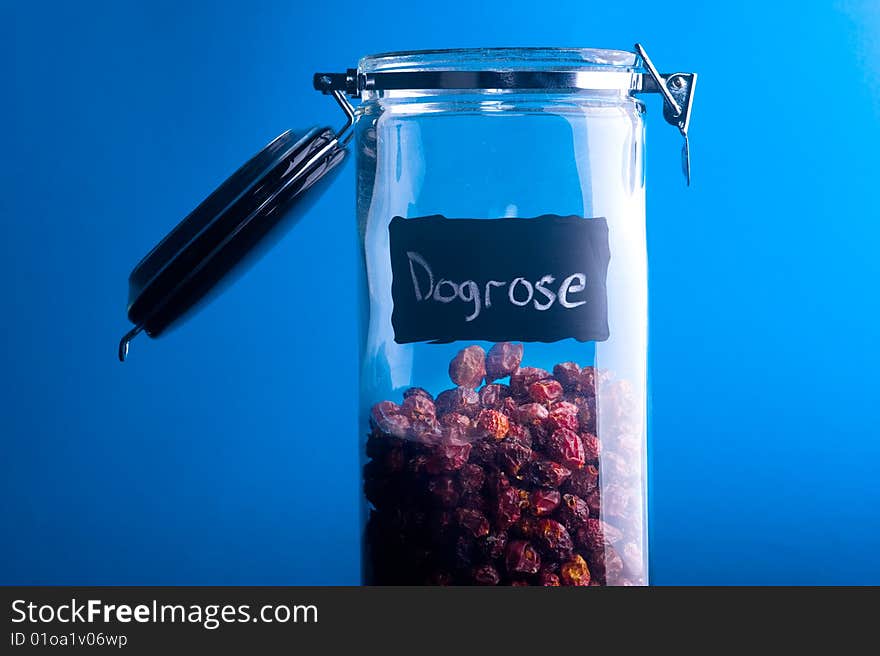 Inscription Dogrose on transparent glass jar. Over blue background