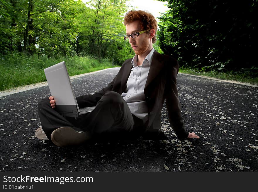 Young man in formal suit using laptop on a country road. Young man in formal suit using laptop on a country road