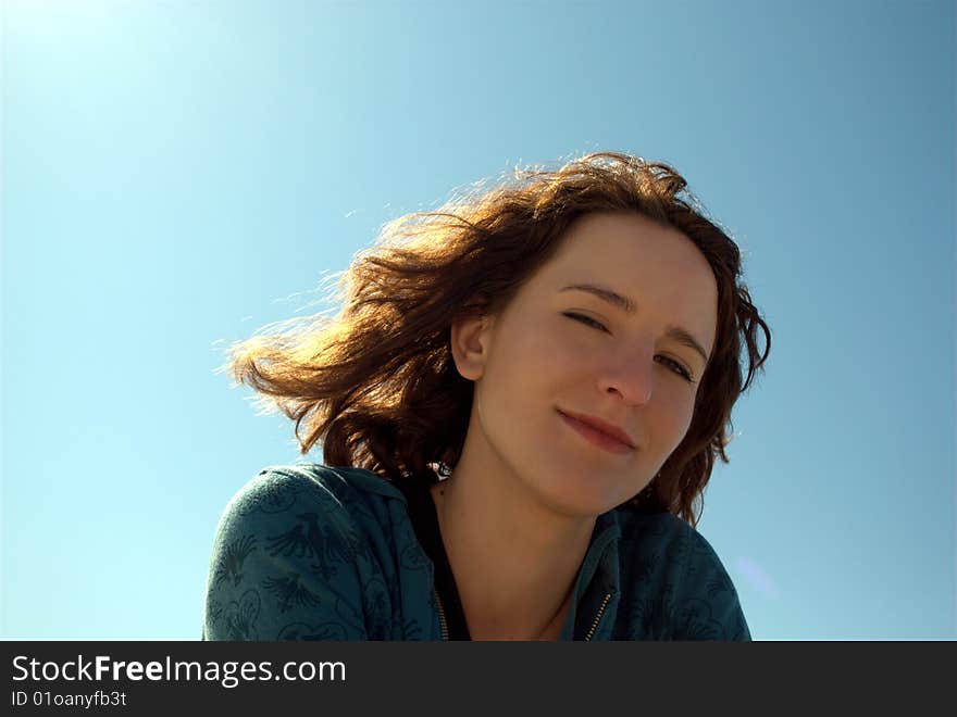 Portrait of a young woman with brown hair, sitting on a beach in a sunny windy day, blinking to the camera, with the sun behind her head. Portrait of a young woman with brown hair, sitting on a beach in a sunny windy day, blinking to the camera, with the sun behind her head.