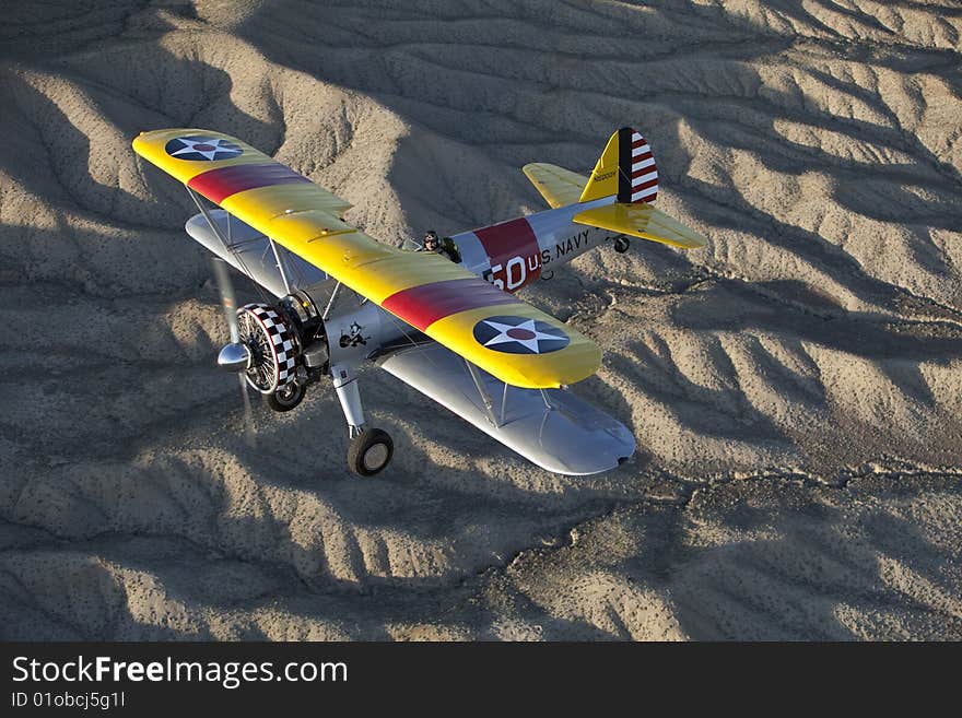 Yellow 1942 steerman flying over rugged desert. Yellow 1942 steerman flying over rugged desert