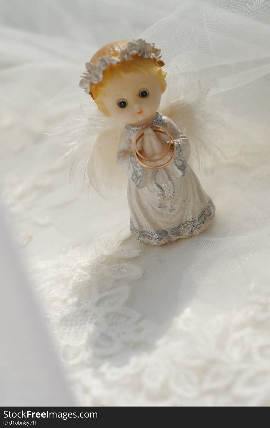 Photo of a figure of a small angel with the wedding rings, standing on a wedding fabric.