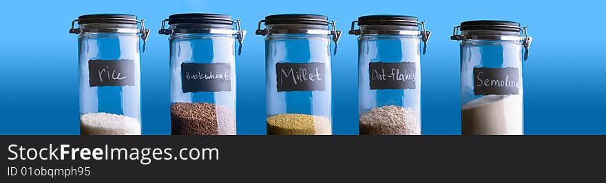 Buckwheat, Rice, Millet, Oat-Flakes, Semolina. Five containers with different groats. Over blue background