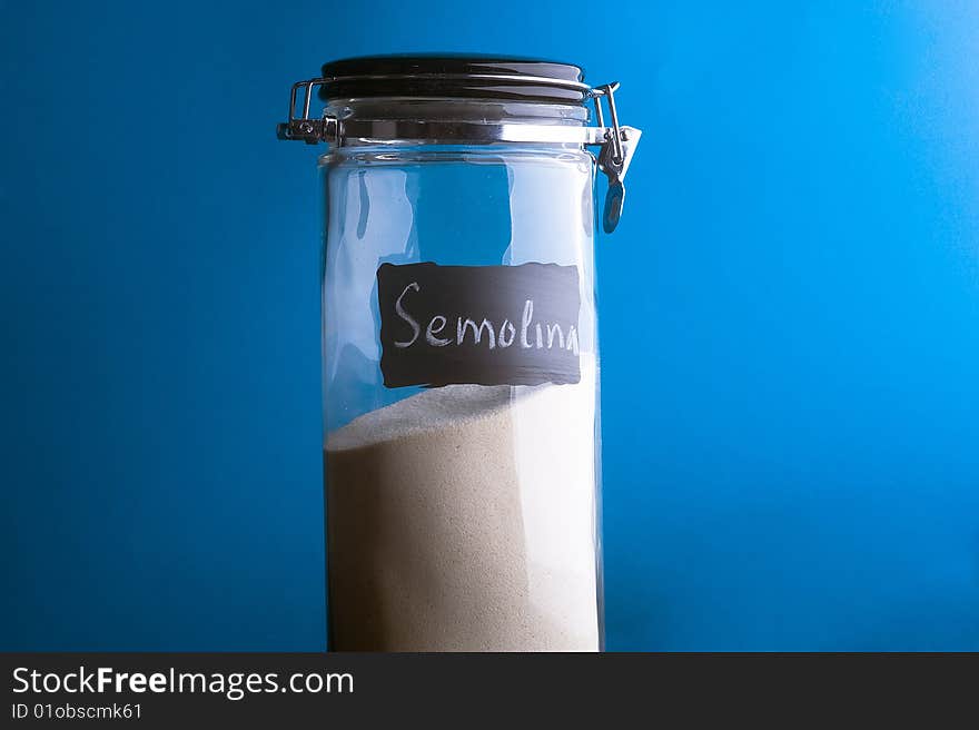 Inscription Semolina on transparent glass jar. Over blue background