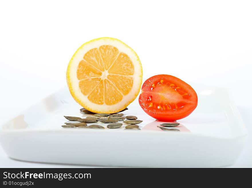 Lemon, tomato and pumpkin seeds on a white plate. Lemon, tomato and pumpkin seeds on a white plate