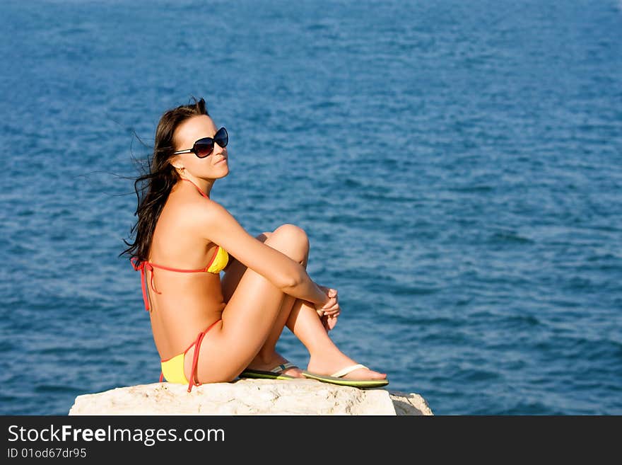 Young beautiful girl sits on the beach of the blue sea