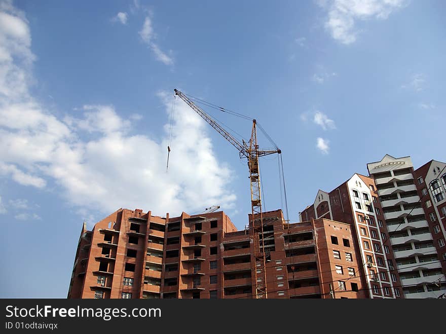 Brick house under construction, tower crane against blue sky. Brick house under construction, tower crane against blue sky